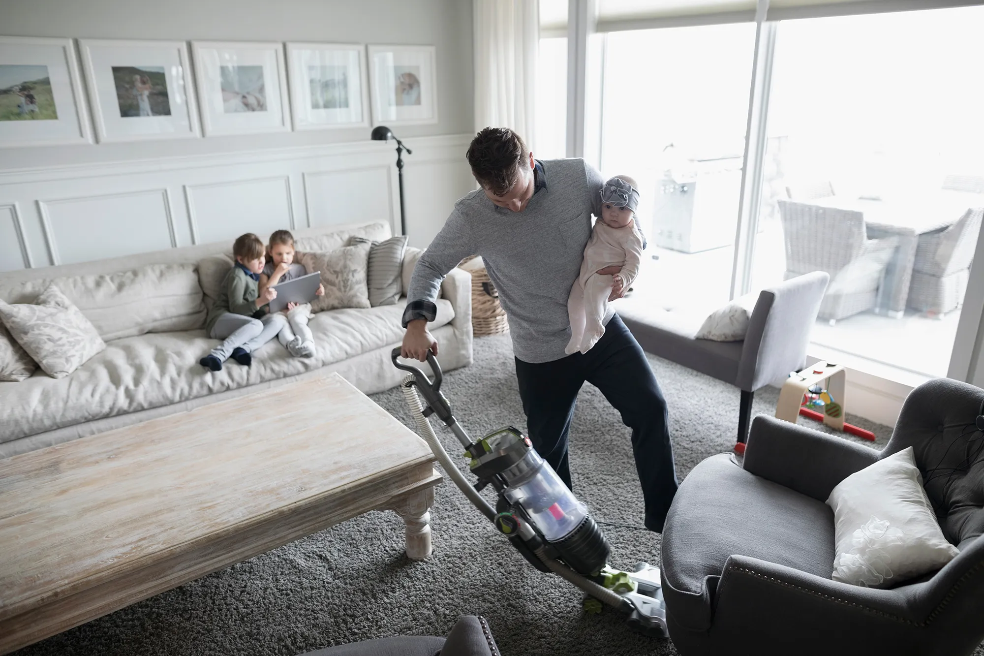 Father holding baby daughter and vacuuming living room