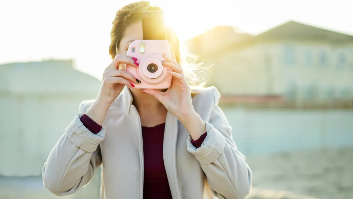 Woman Holding Instant Camera While Standing At Beach