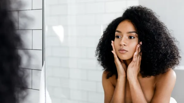 Mixed race woman massaging her face and looking at a mirror