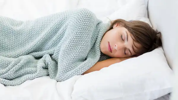 woman sleeping in bed on white pillow with a blue blanket