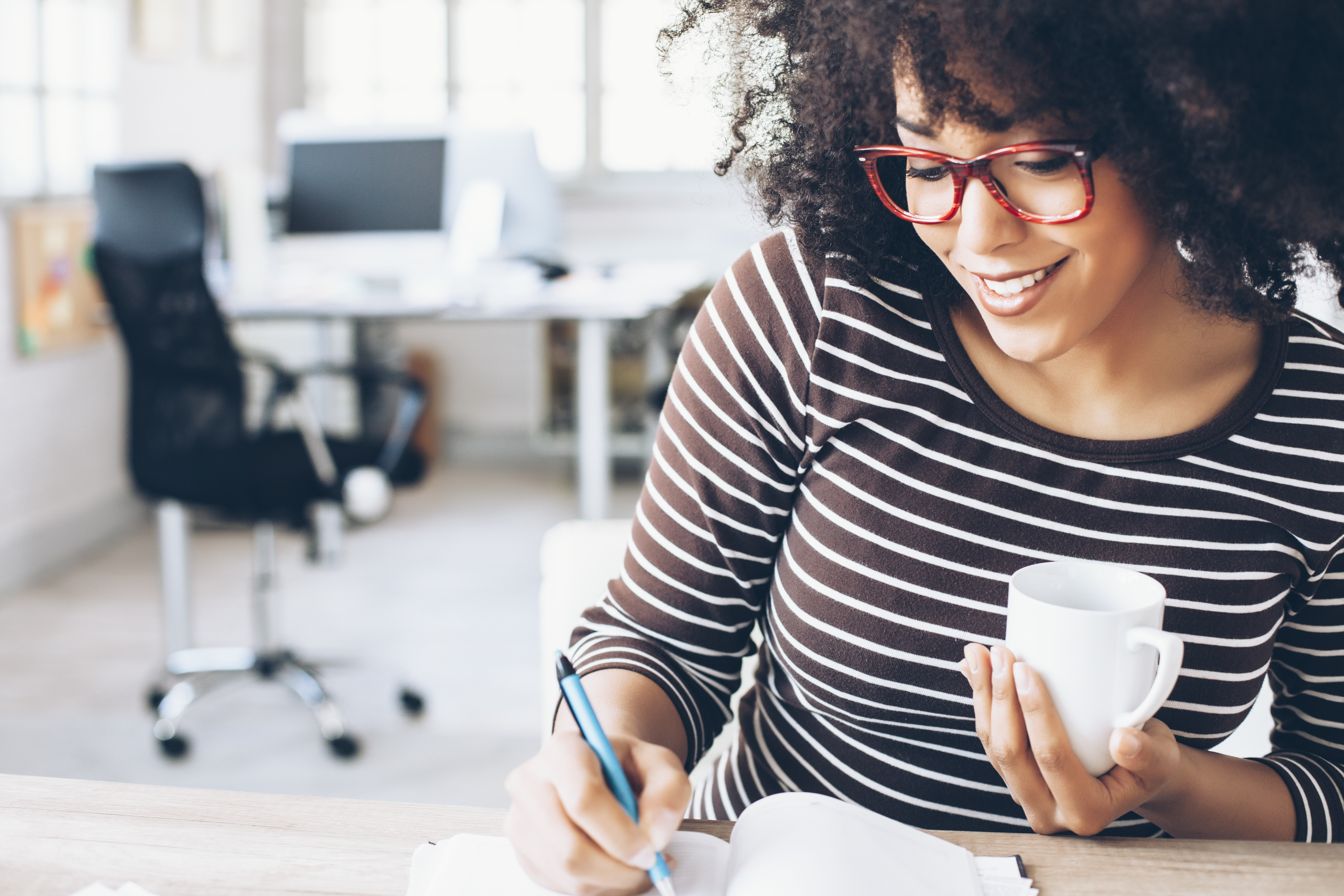 woman sitting at desk working with curly hair, red glasses, office chair