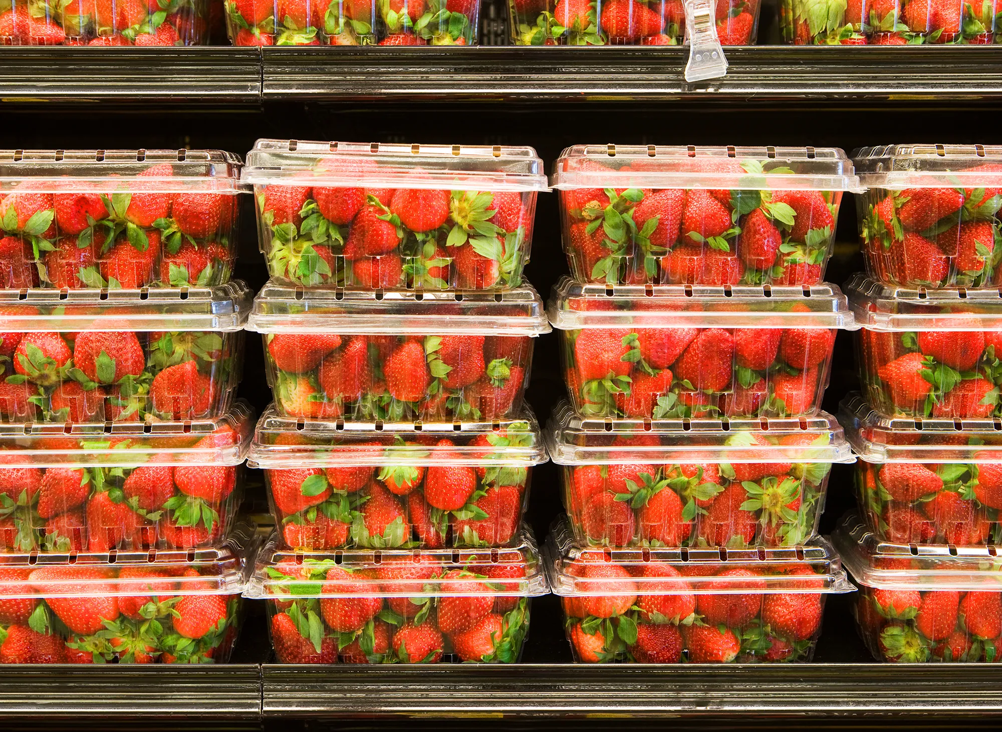 Strawberries in containers on supermarket shelf.