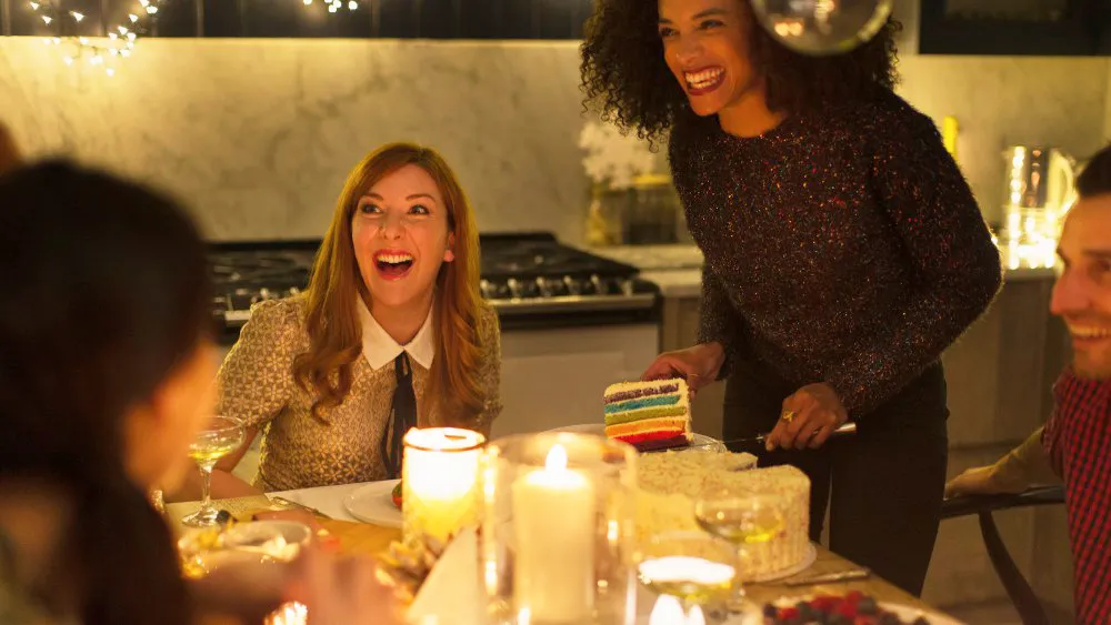 Laughing friends enjoying cake at candlelight Christmas dinner party