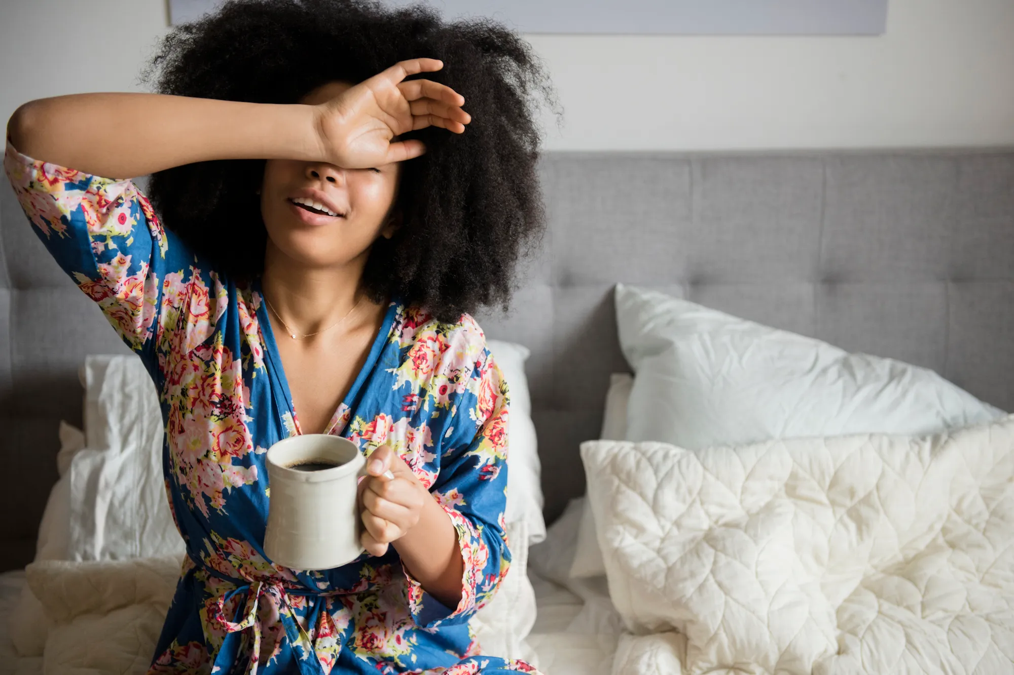 African American woman sitting in bed drinking coffee