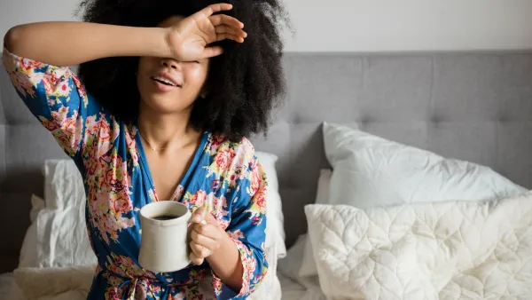 African American woman sitting in bed drinking coffee