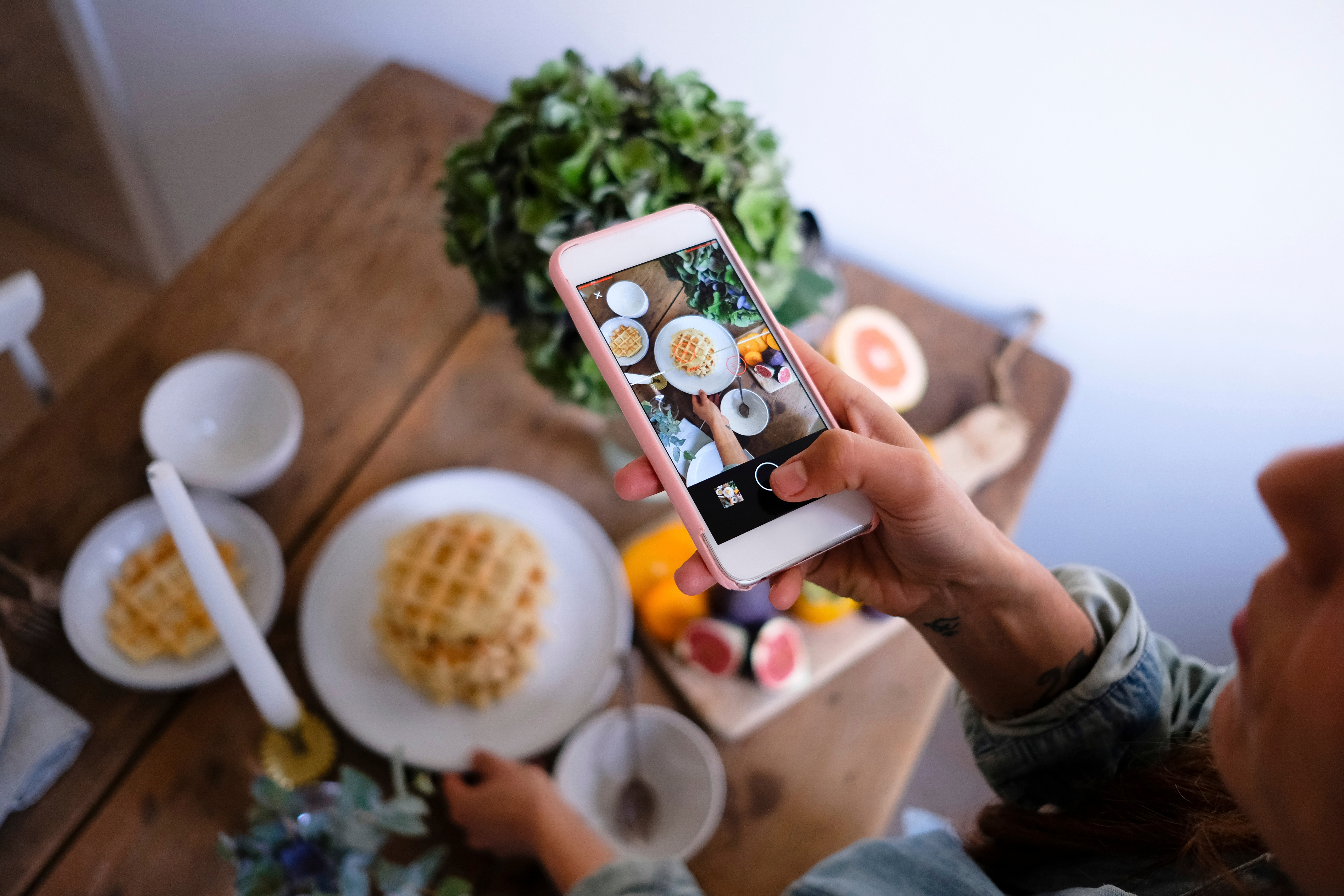 High angle view of woman photographing waffles in plate on table at home