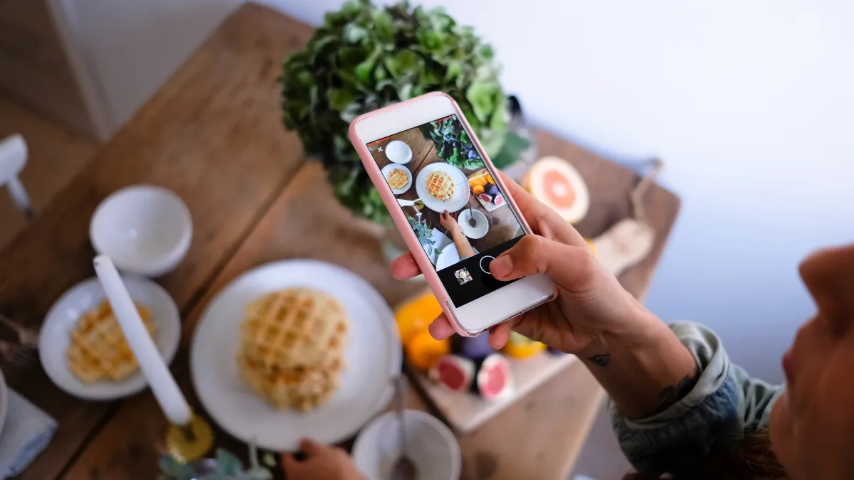 High angle view of woman photographing waffles in plate on table at home