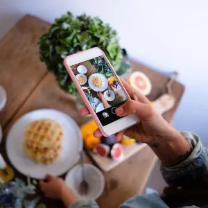 High angle view of woman photographing waffles in plate on table at home