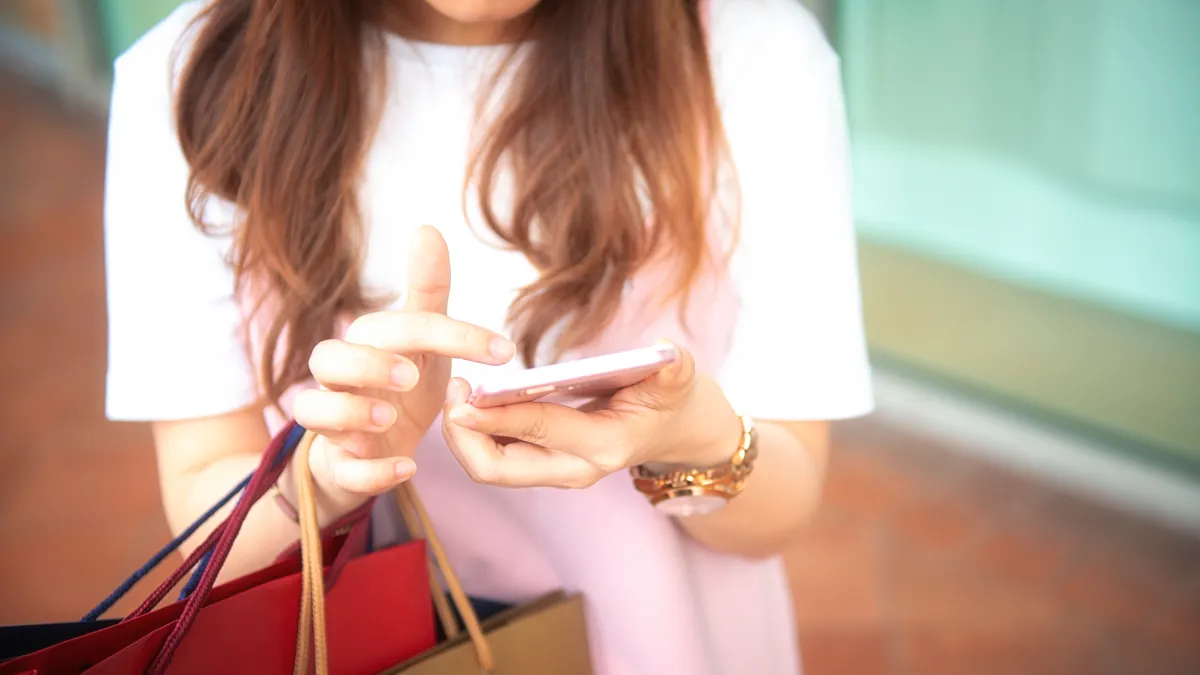 Midsection Of Woman Using Phone While Holding Shopping Bags On Footpath