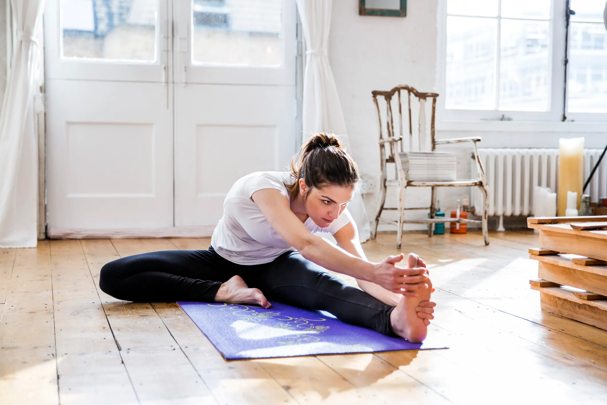 Young woman practicing yoga, touching toes in apartment