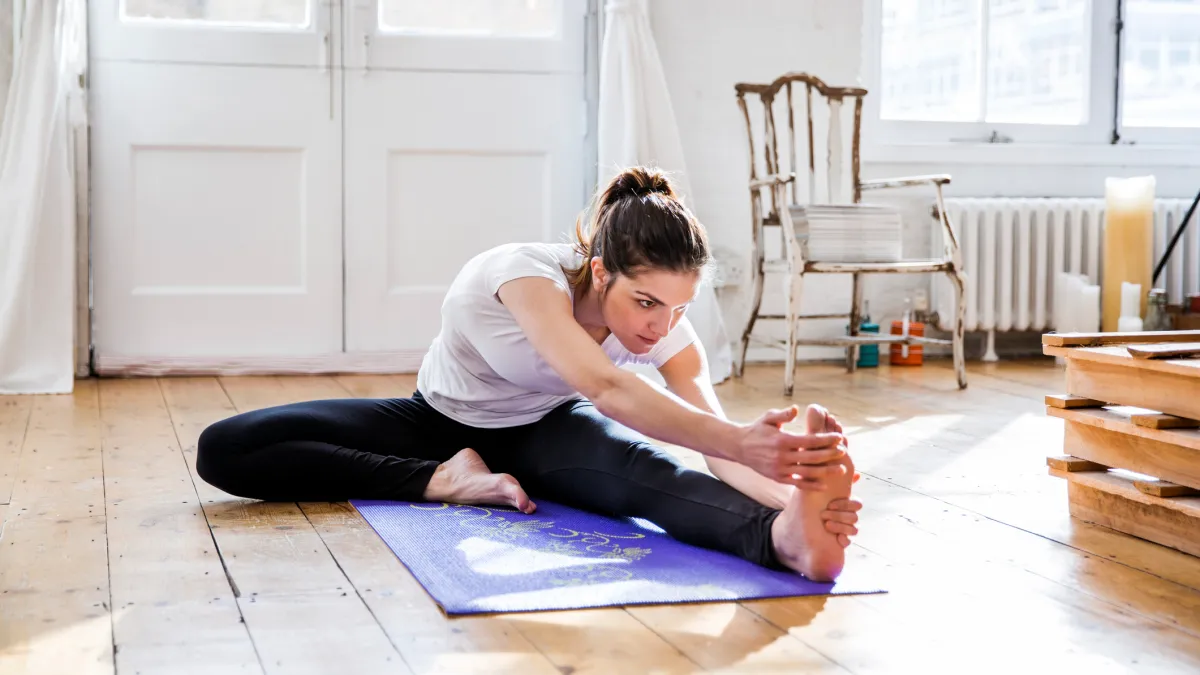 Young woman practicing yoga, touching toes in apartment