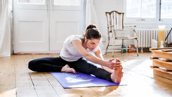 Young woman practicing yoga, touching toes in apartment