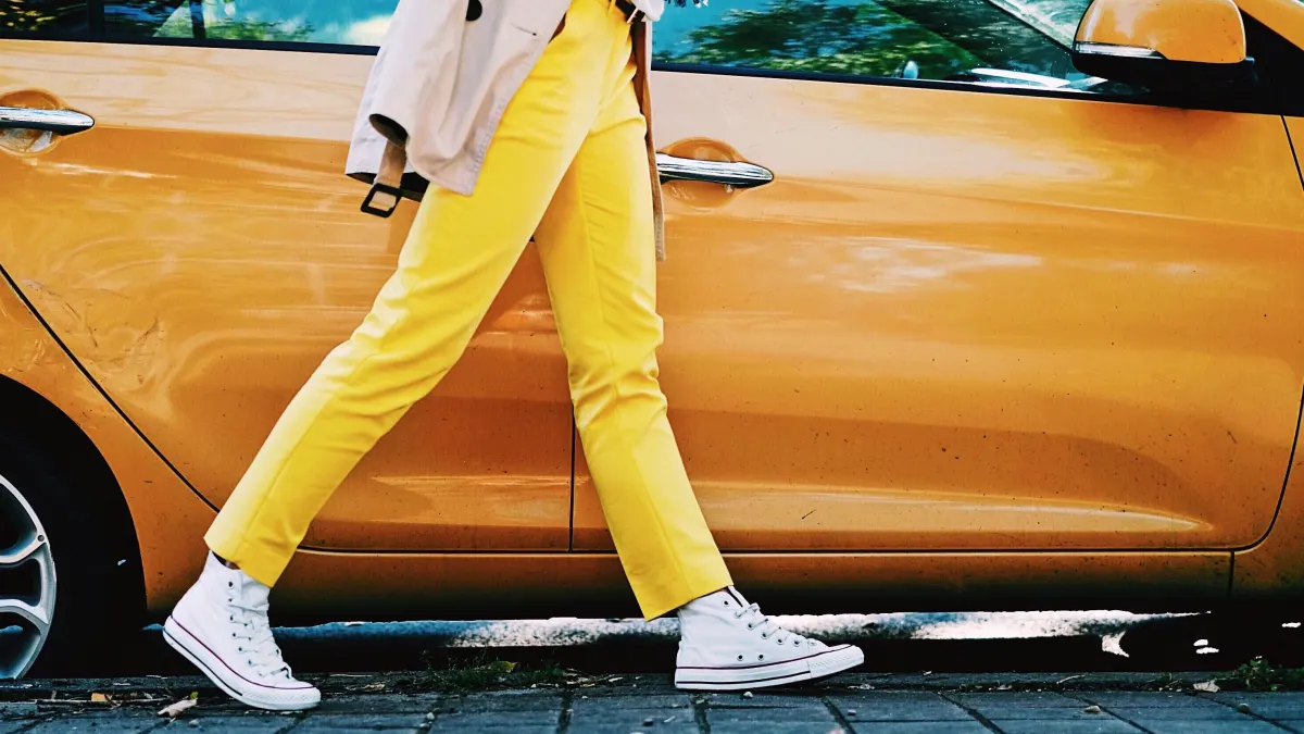 Woman in yellow trousers walking past an orange car