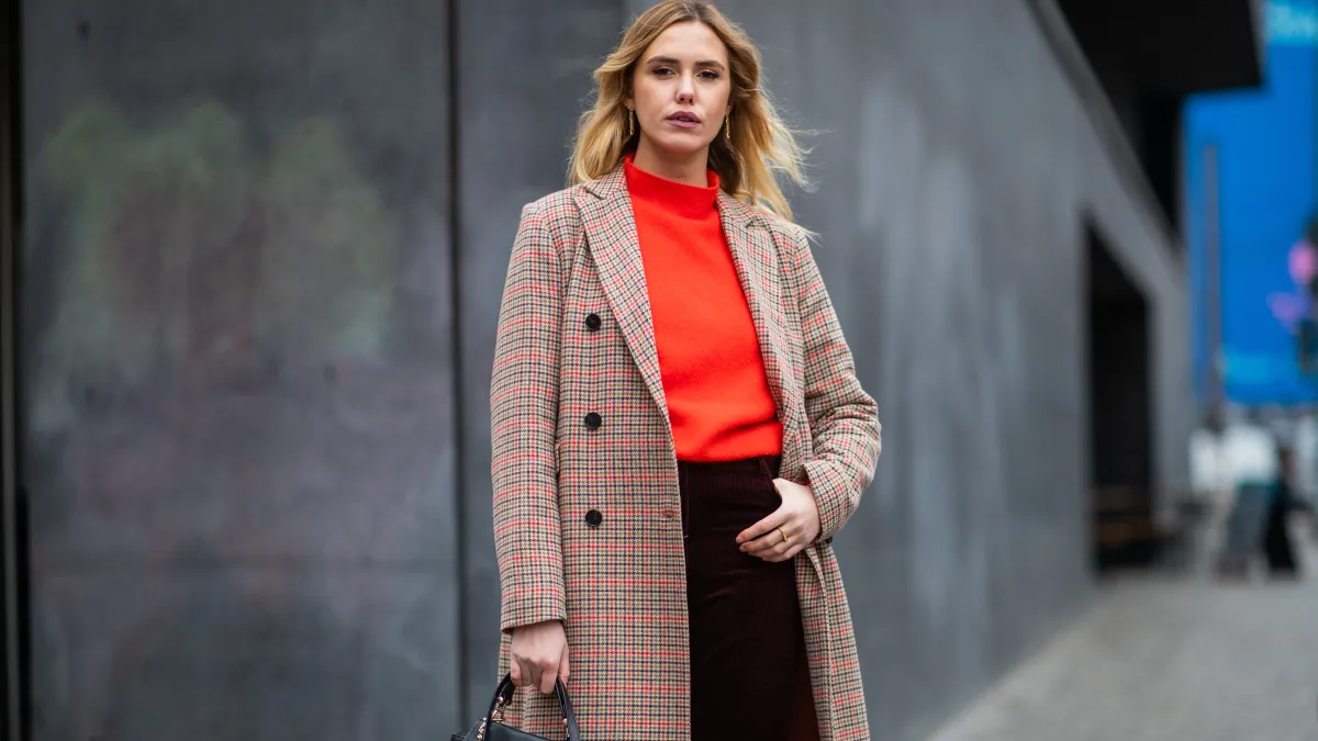 woman wearing a plaid coat with a red turtleneck and a black skirt and a black bag