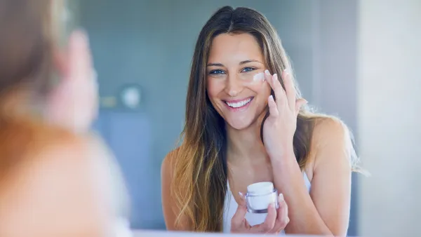 Portrait of a beautiful young woman applying moisturizer to her face while looking in the mirror