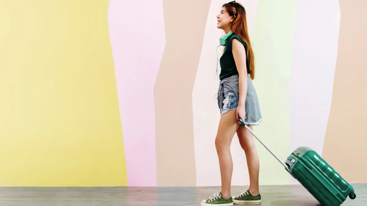 Woman With Wheeled Suitcase Standing Against The Wall
