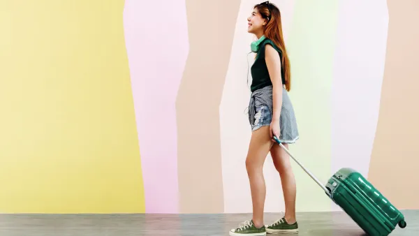 Woman With Wheeled Suitcase Standing Against The Wall