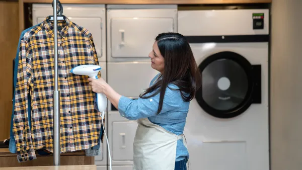 Woman working at a laundry service using a garmet steamer on shirt - Business industry concepts