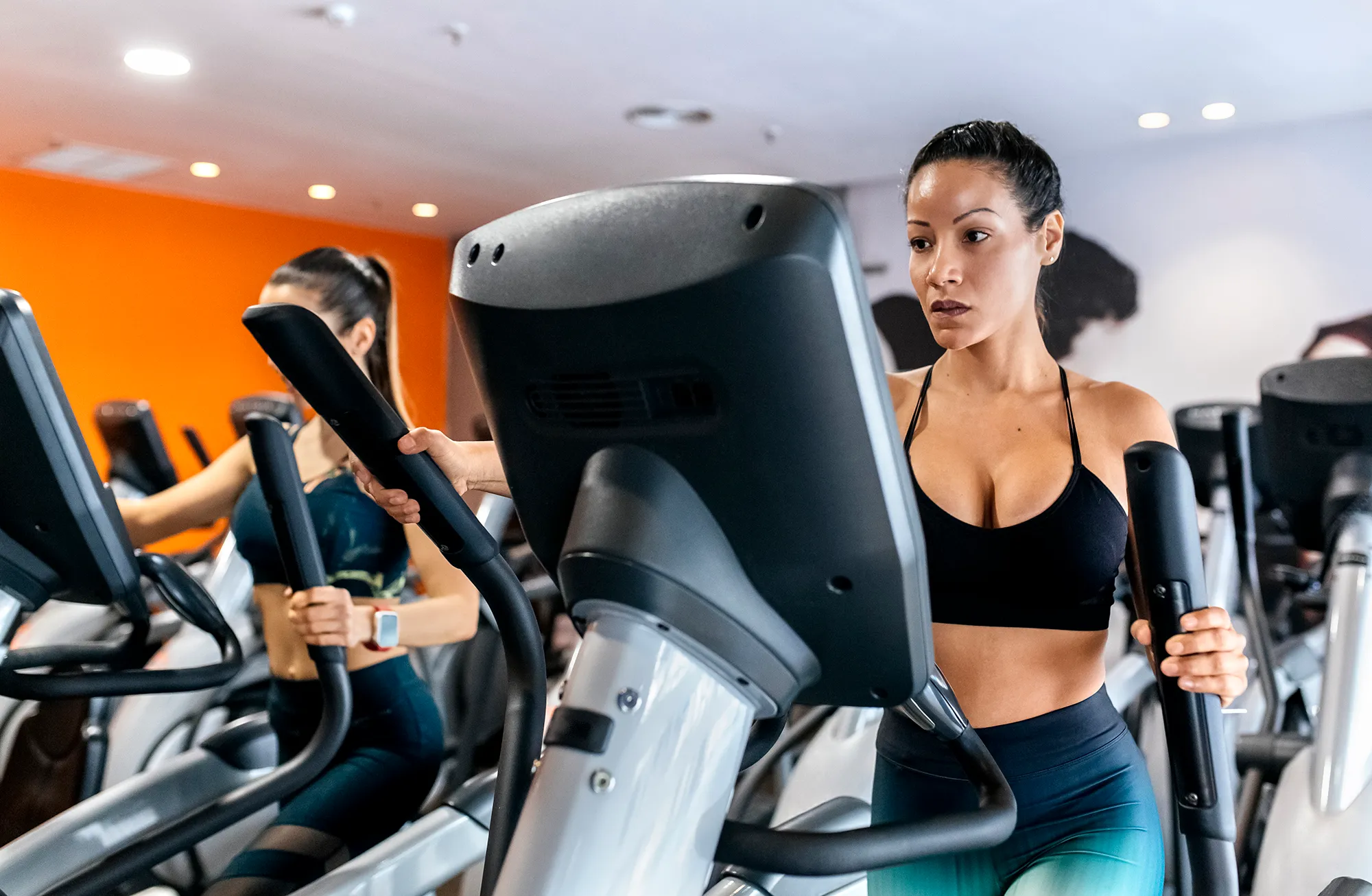 two women working out in gym using a elliptical