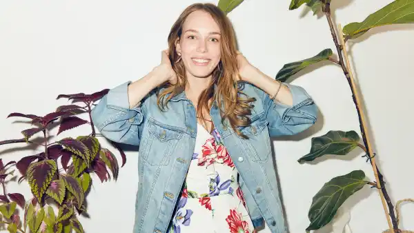 Portrait of smiling young woman with hands in hair standing amidst plants against white wall at home