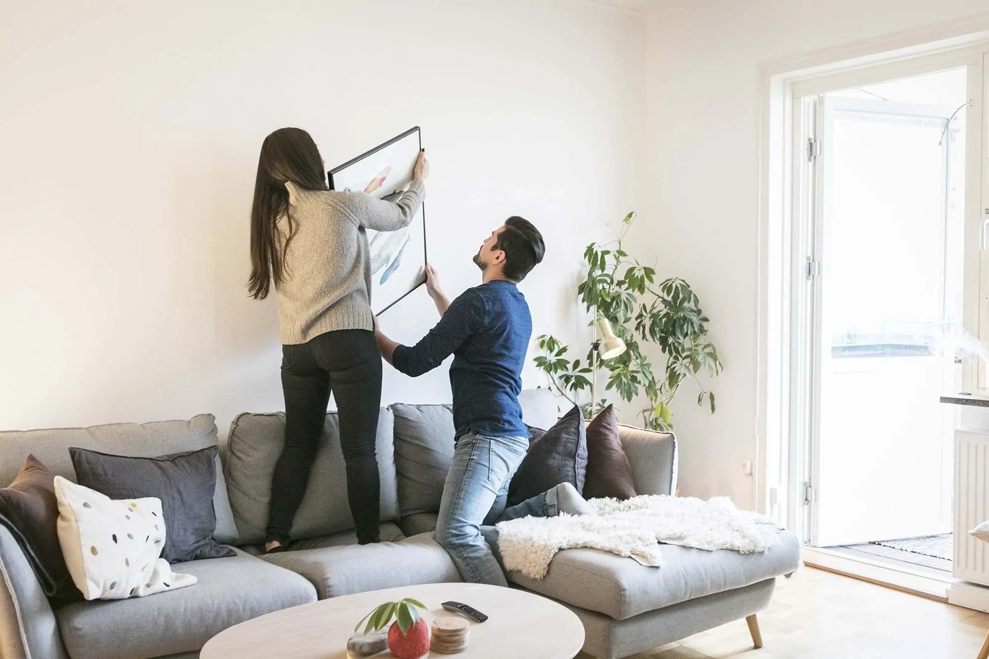Couple adjusting painting on wall while leaning on sofa at home