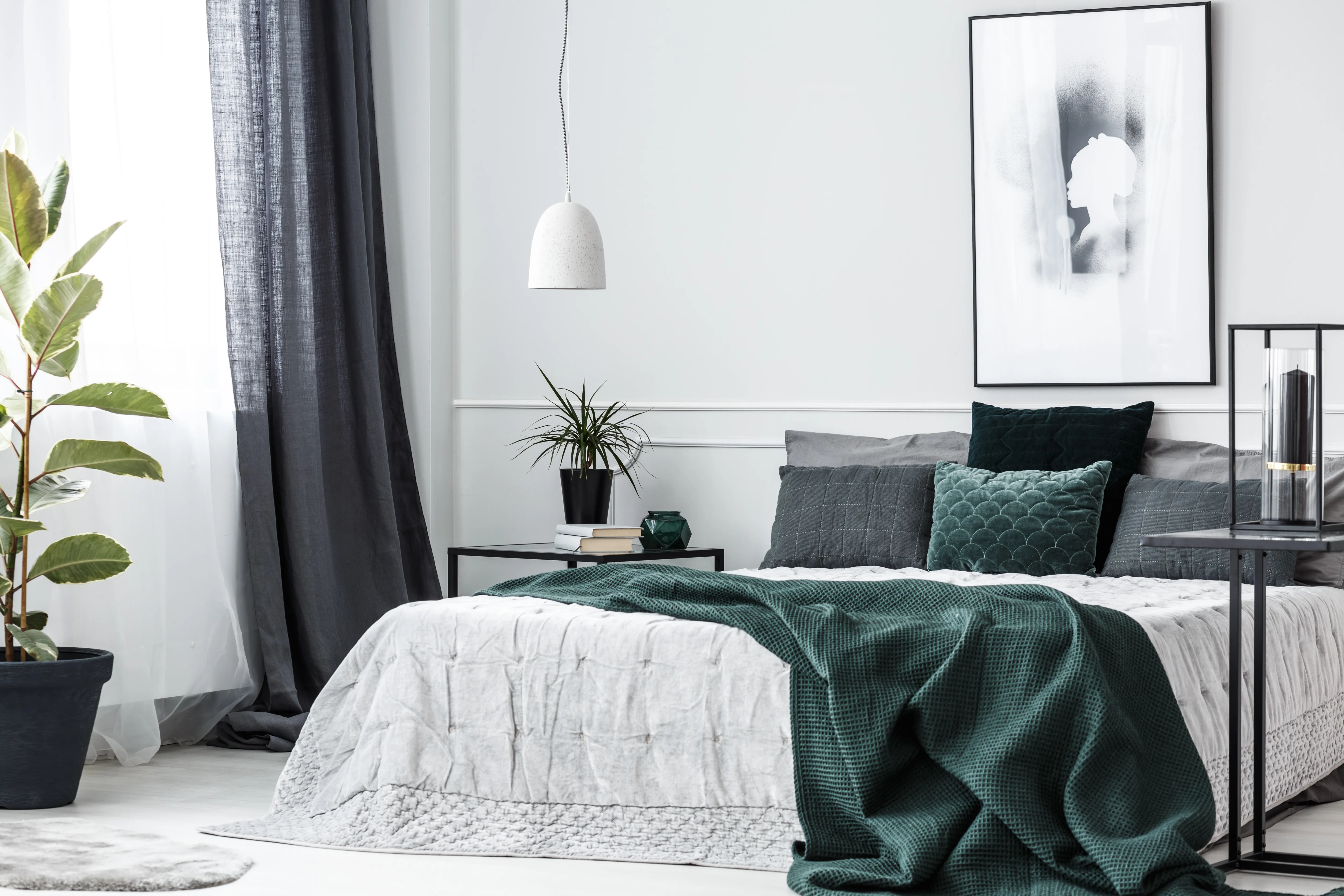 Green blanket on bed in elegant bedroom interior with poster on white wall and plant on table