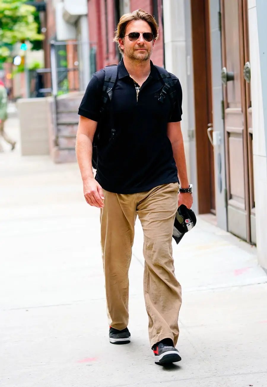 Bradley Cooper Walking in NYC Wearing Khaki Pants Blue Shirt Backpack Sunglasses and Holding A NFL Super Bowl Champions Hat