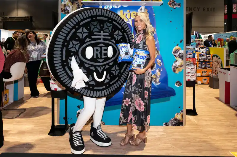 Giuliana Rancic special appearance with Cookie Pop and Candy Pop at the Sweets and Snacks Show in Chicago, as she poses with the Cookie Pop OREO mascot and the Sour Patch Kids mascot, enjoying the popcorn treats.