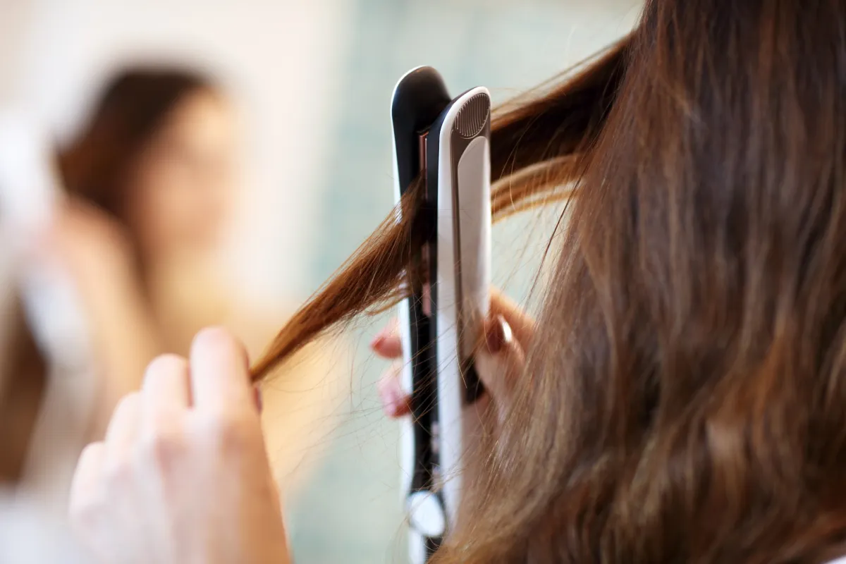 A woman using one of the best flat irons of 2023 to straighten her hair.
