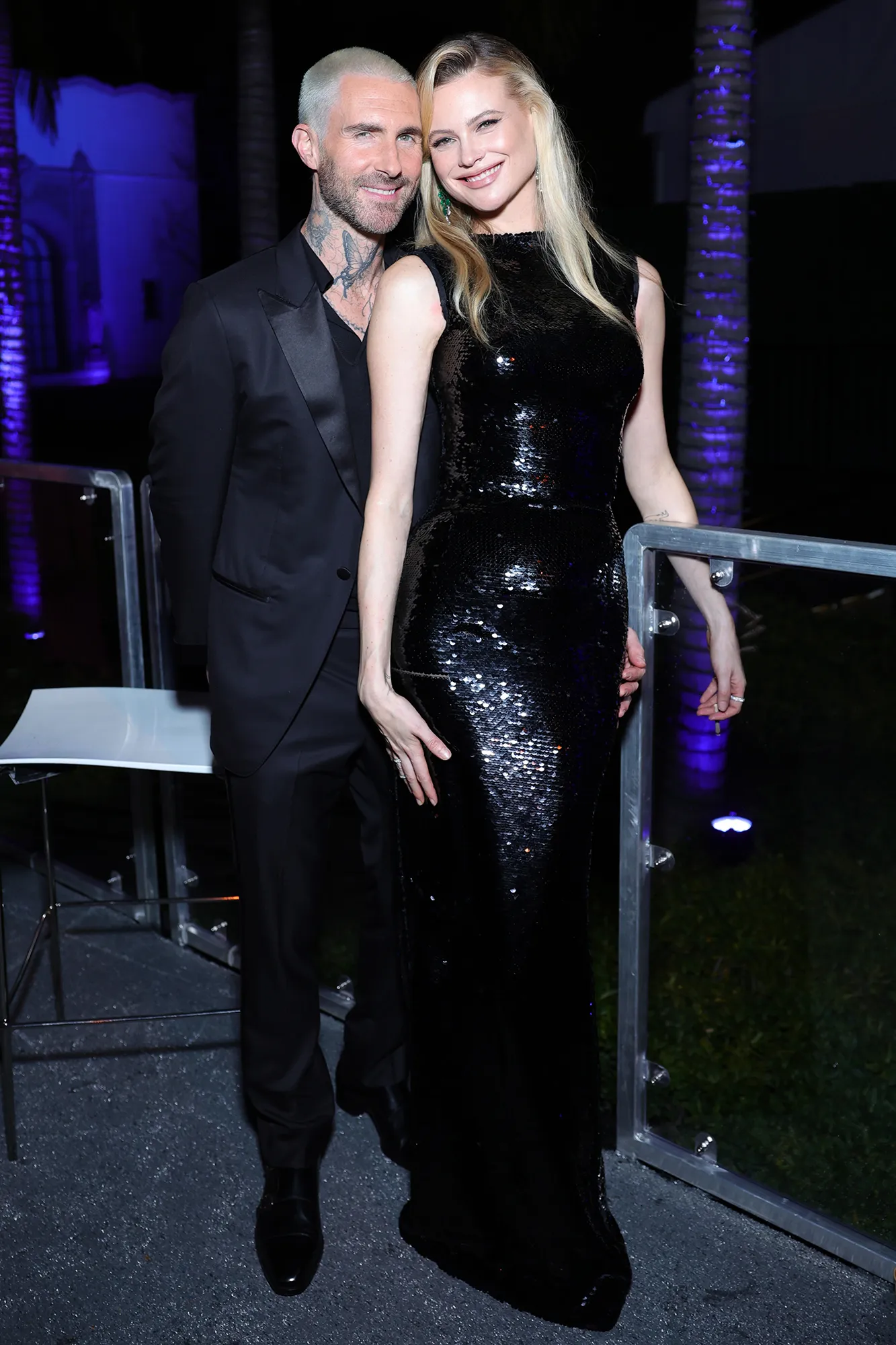 Adam Levine wears a black suit with Behati Prinsloo wearing a black sequin dress as they smile and pose at the Vanity Fair Oscar Party
