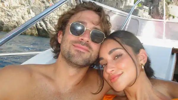Greg Grippo shirtless, wearing sunglasses with arm around Victoria Fuller wearing orange bikini as they smile on a boat on the Amalfi Coast