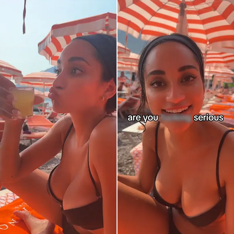 Victoria Fuller wearing black bikini holds a shot on the beach with orange and white striped umbrellas