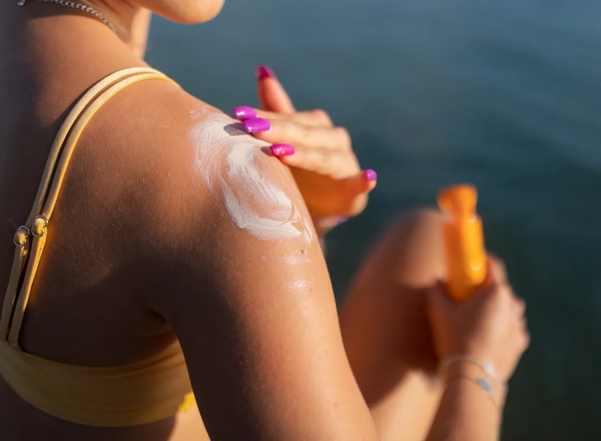 Close-up of young woman in yellow swimsuit applying suncreen on her skin, vacation and skin protection concept.