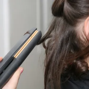 A woman using one of the best flat irons of 2023 to curl her hair.