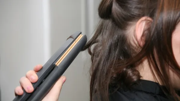 A woman using one of the best flat irons of 2023 to curl her hair.