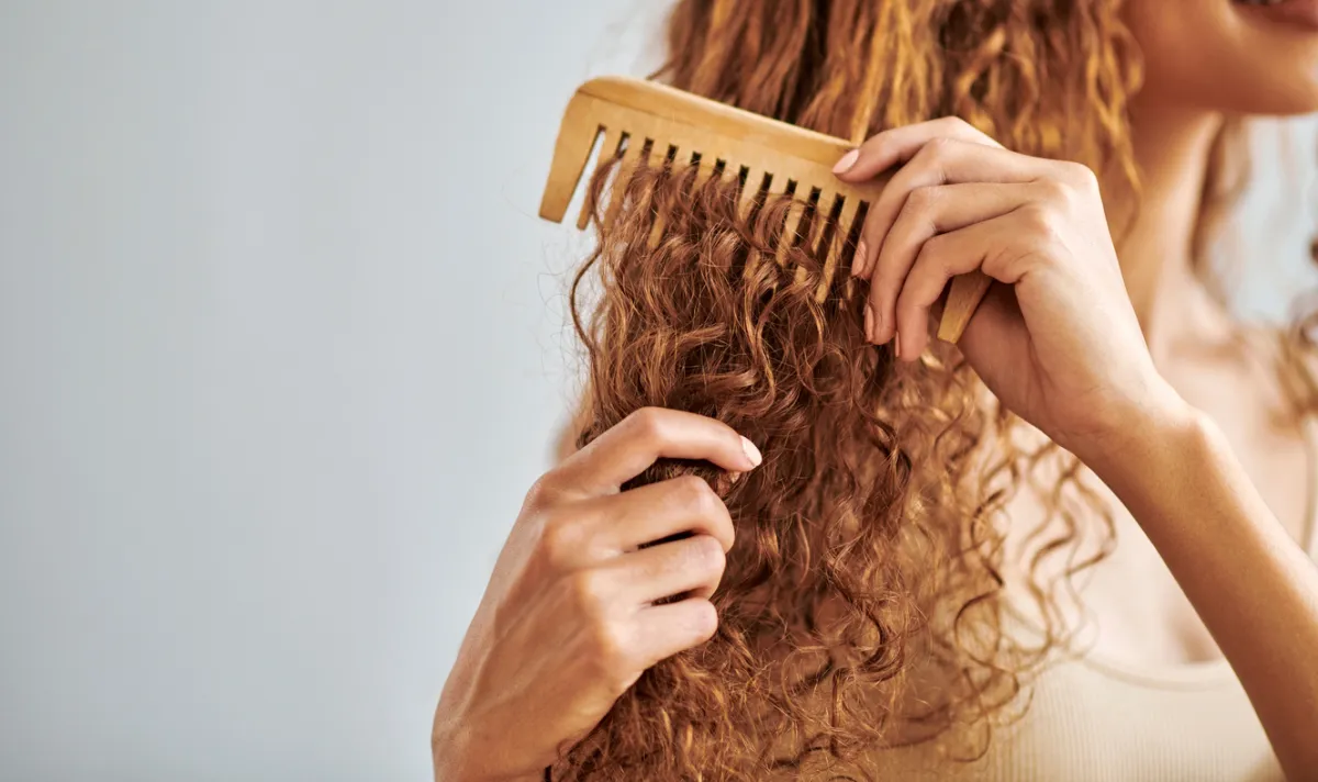 A woman with curly, red hair combs in leave-in conditioner