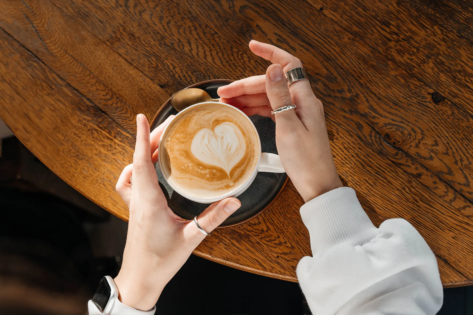Cappuccino in a white ceramic cup with women's hand on a wooden table. Top view.