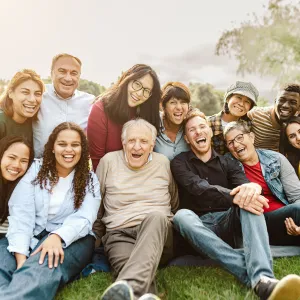 Happy multigenerational people having fun sitting on grass in a public park