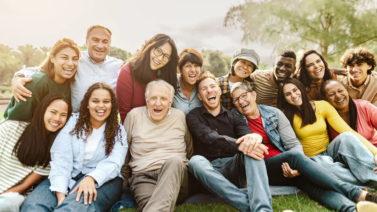 Happy multigenerational people having fun sitting on grass in a public park