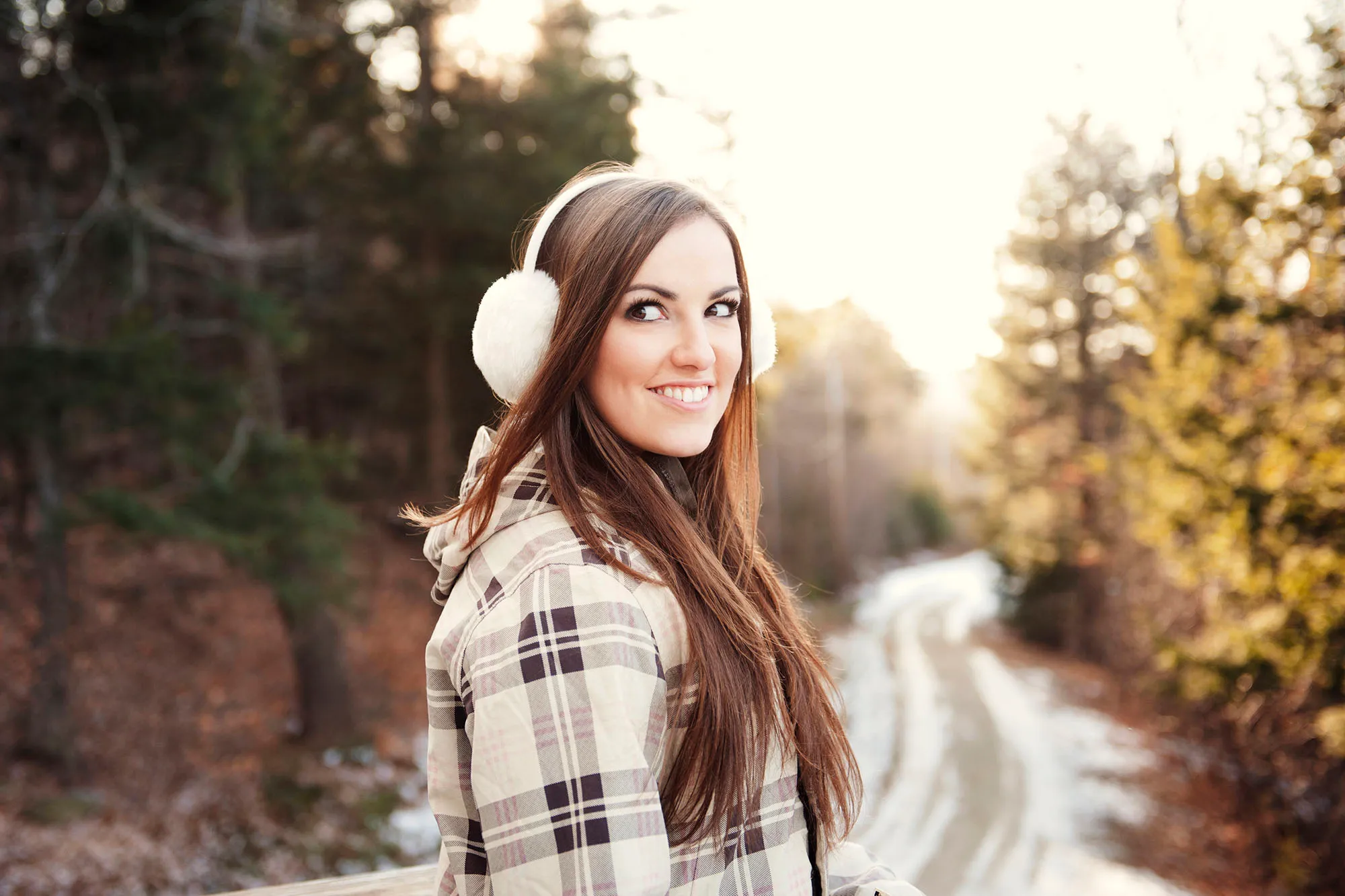 Happy woman wearing ear muff while standing on footpath during winter