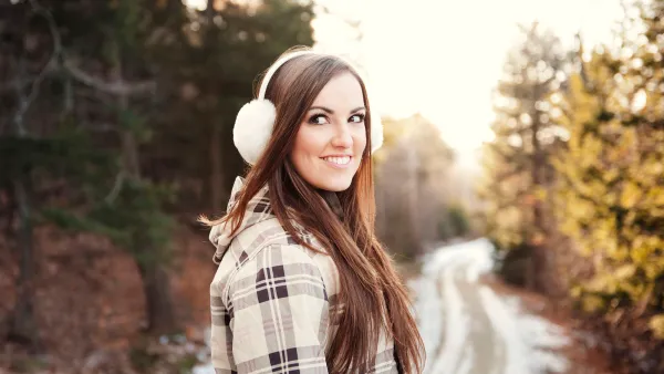 Happy woman wearing ear muff while standing on footpath during winter