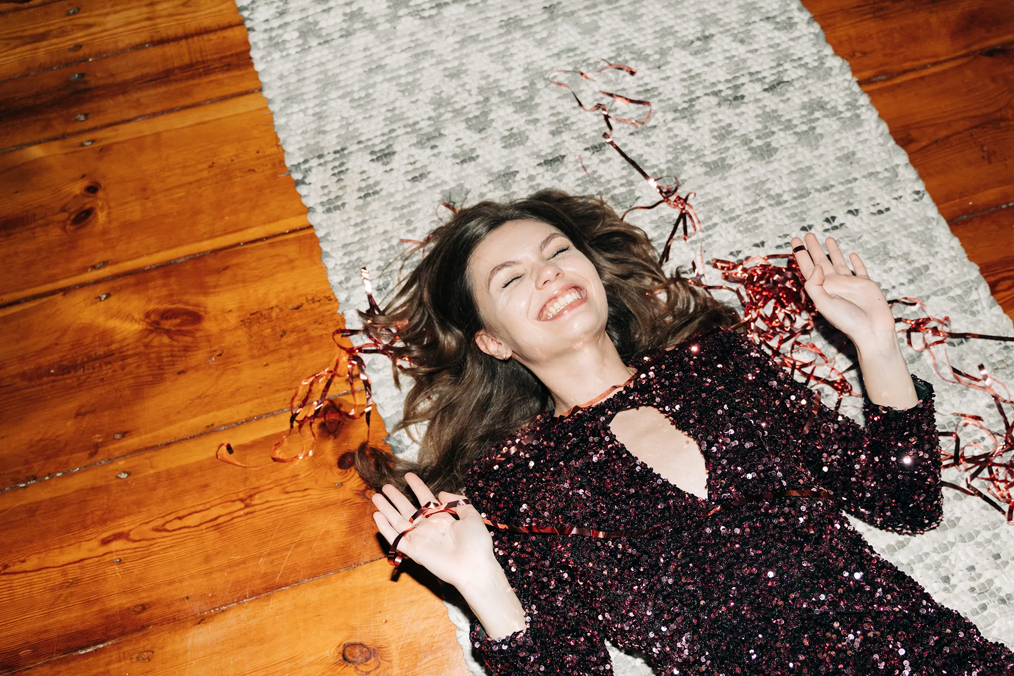 Happy young woman in glittering cocktail dress on carpet floor, flash light, user generated content