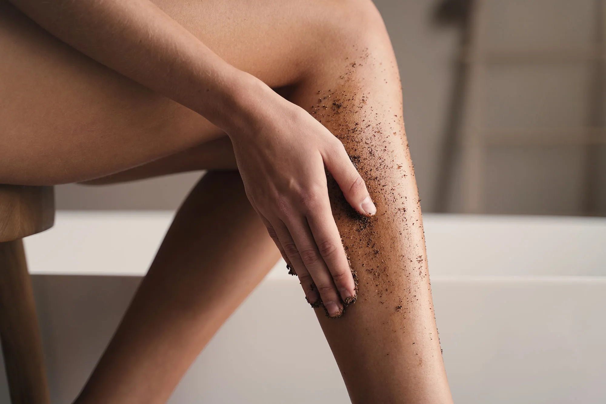 Crop shot of woman hand scrubbing legs with organic scrub in bathroom during anti-cellulite massage. Body and skin care. peeling and exfoliating procedure