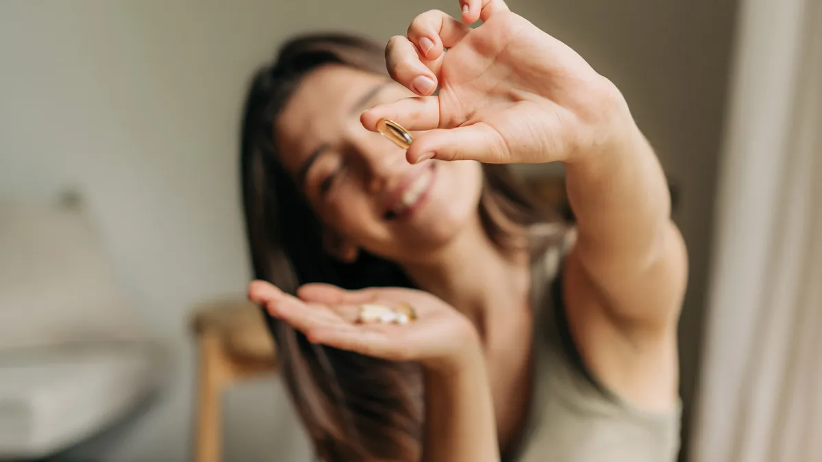 Happy smiling woman holding an omega pill in her hand.