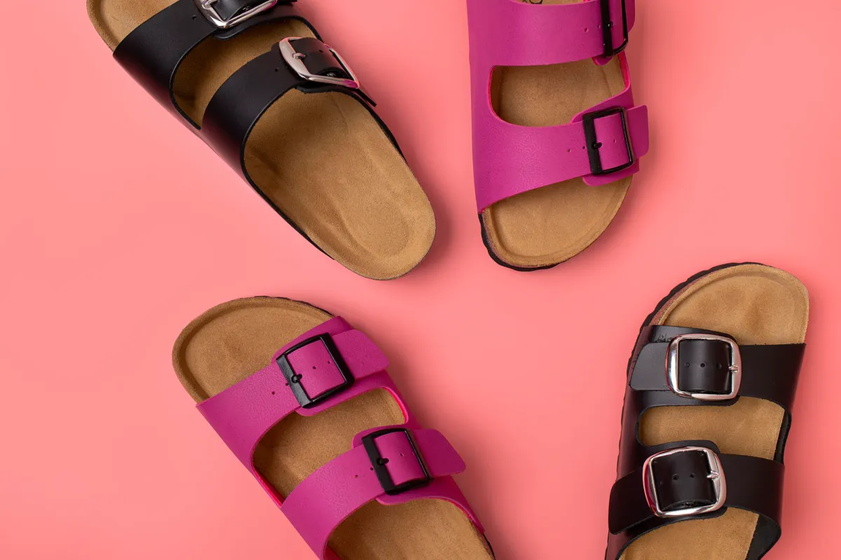 Trendy fashion footwear mockup. Leather pink and black sandals birkenstocks on pink background top view flat lay. Unisex summer shoes, genuine leather flip flops with cork soles