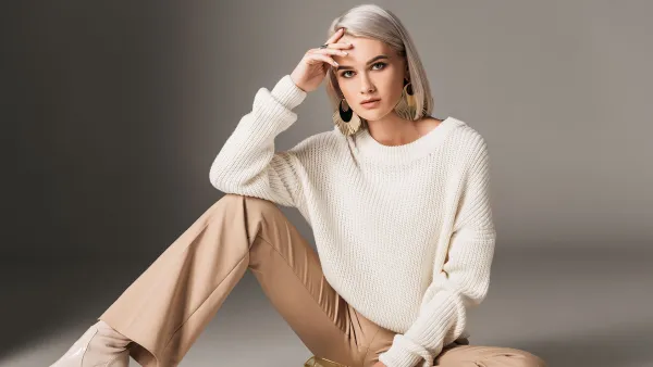 attractive fashionable woman posing in white trendy sweater, beige pants and autumn heels, on grey