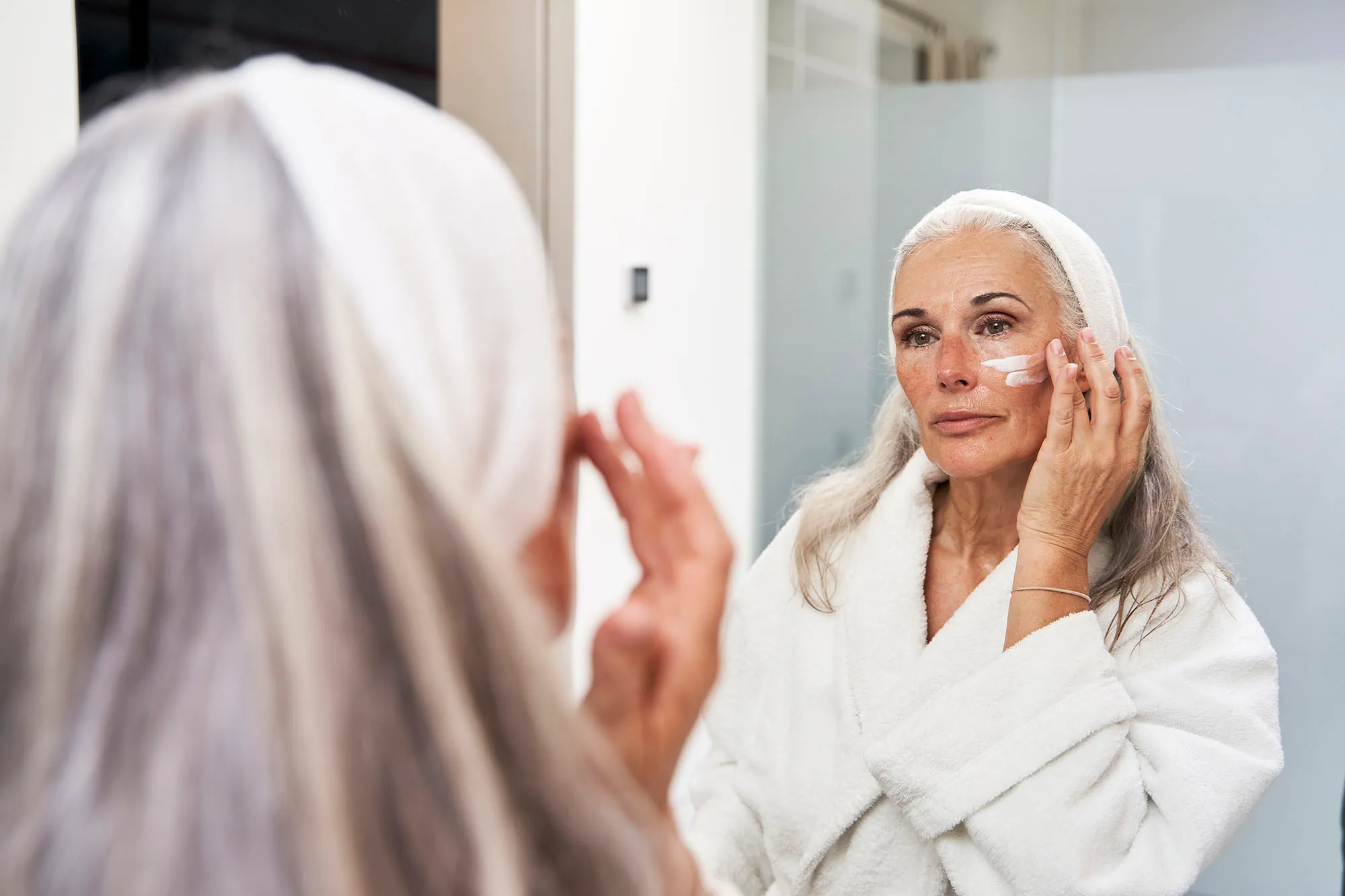 Mature woman applying face cream in bathroom