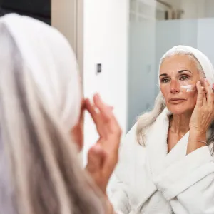 Mature woman applying face cream in bathroom