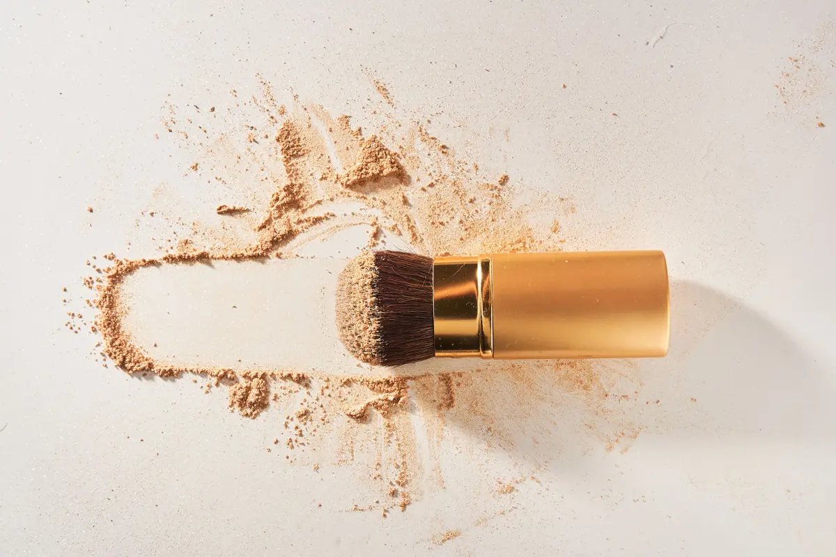 Soft cosmetic brush, with shining sparkling powder on the bristles.The powder is scattered on the table, on a light background with space to copy in the concept of beauty and makeup.High quality photo