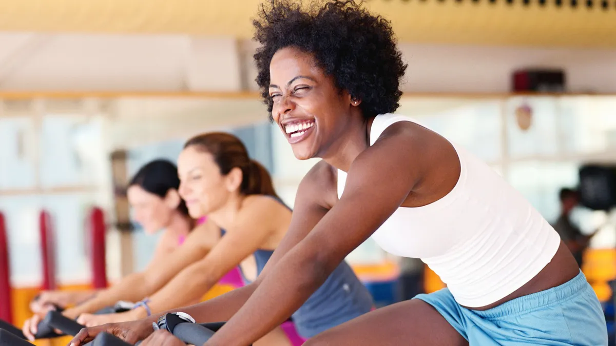 Women sitting on exercising bikes in gym, side view